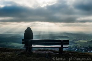 eine Frau sitzt auf einer Bank und blickt in eine weite Landschaft